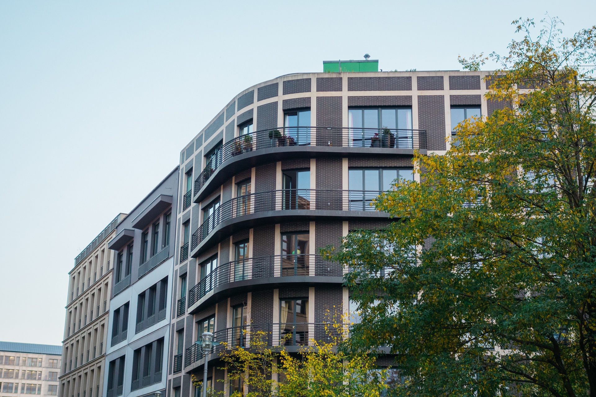 Two people are lying on massage tables, covered with dark towels. A person in a white robe stands nearby, holding a glass. The setting appears to be a spa or relaxation room.